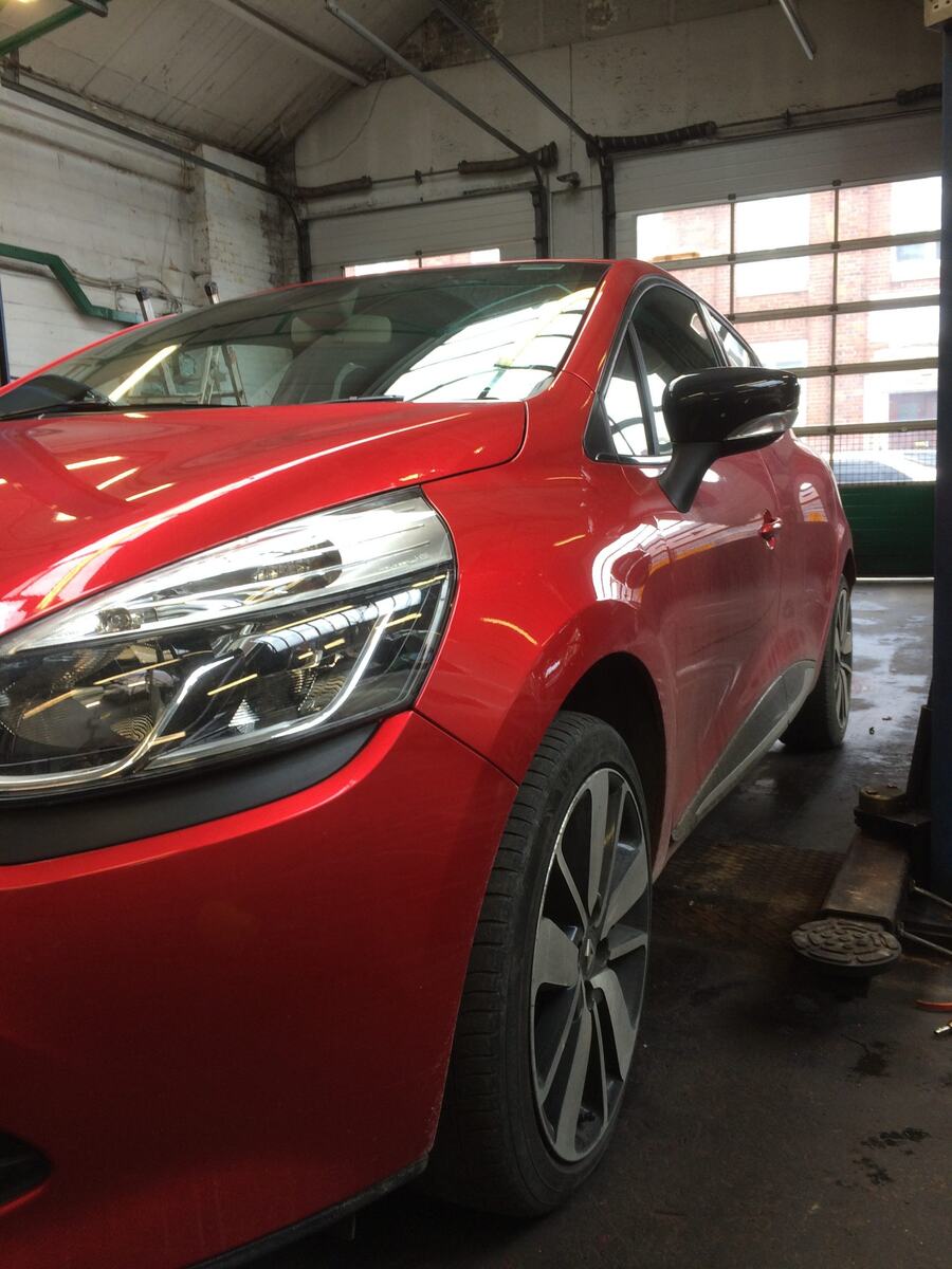 Front three-quarter view of a red Renault Clio in the workshop